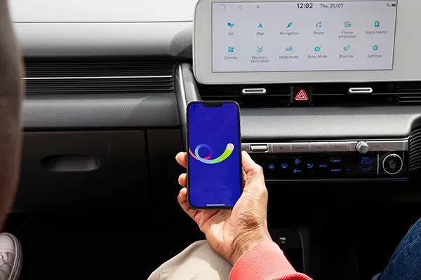 A smartphone displaying the bp pulse app held inside a car, with the vehicle’s dashboard and infotainment screen visible in the background.