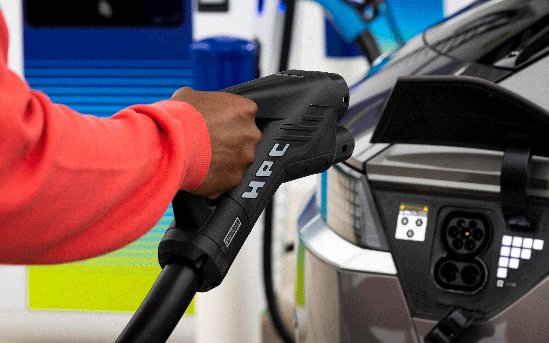 A hand holds the connector end of a charging cable, as they go to plug their electric vehicle in to a bp pulse charger. 