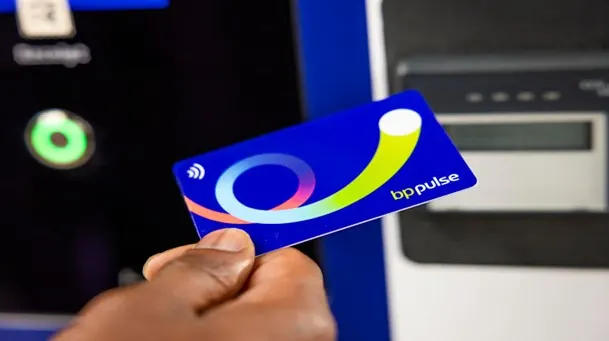 A close-up image of a hand holding a bp pulse card near an electric vehicle charging station, showcasing the contactless payment feature for convenient EV charging.