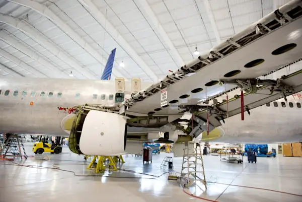 Aircraft undergoing heavy maintenance with open panels inside a hangar.