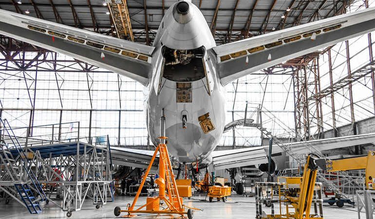 Aircraft in heavy maintenance with multiple technicians working across the fuselage and wing.