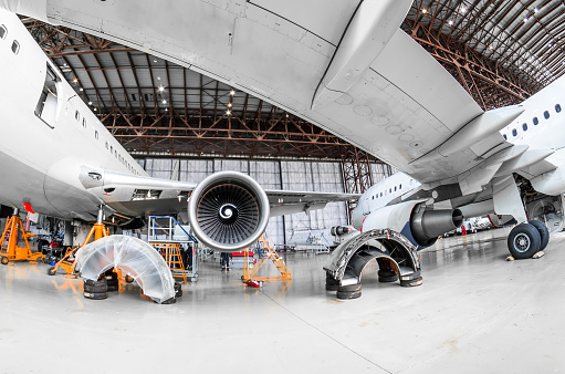 Wide shot of multiple aircraft undergoing maintenance inside a large hangar.