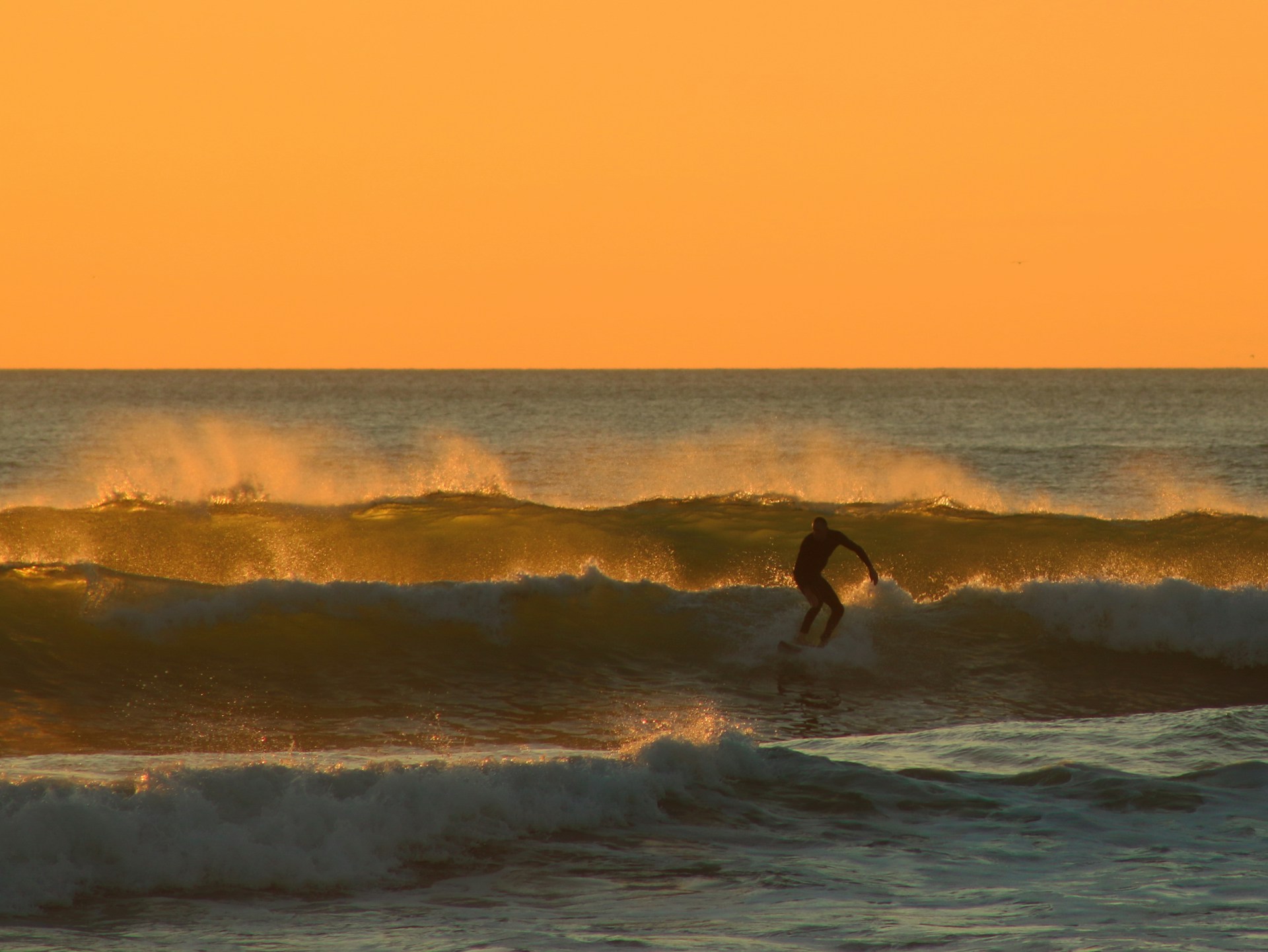 Man surfing at dusk | A man surfing small waves at dusk.