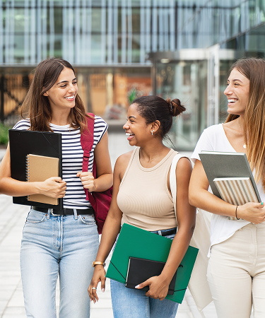 Four smiling young women walking together outdoors on campus holding study notebooks, representing daily freshness and active lifestyles