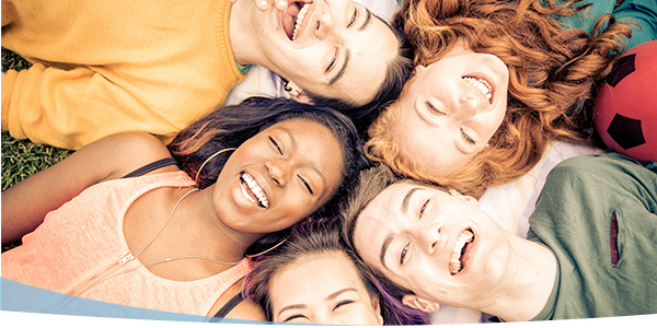 Group of five smiling friends lying on the grass, enjoying a sunny day together, with a soccer ball nearby