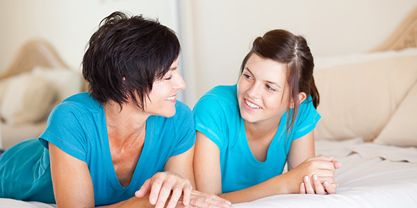 Mother and daughter in blue t-shirts lying on the bed and smiling.