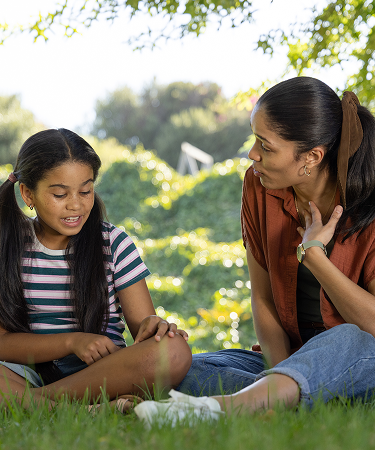 A young girl and a woman share a tender moment outdoors, showcasing a bond of love and connection between them