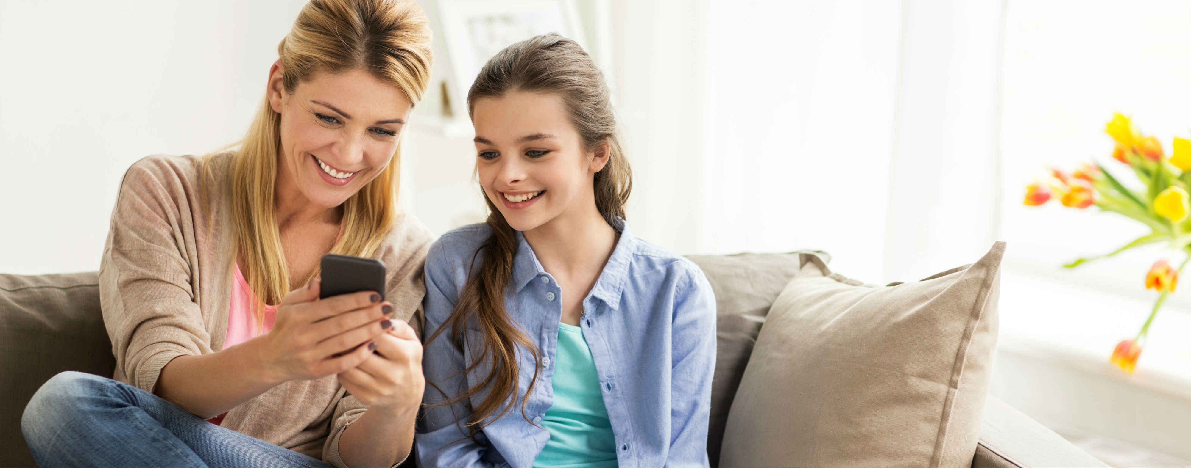 Mother and daughter sitting on a couch looking at a cell phone.