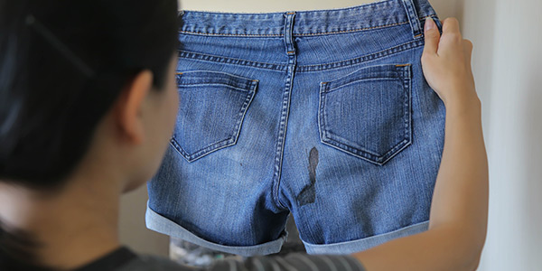 A person inspects a pair of blue denim shorts stained with a dark mark, hanging on a wall