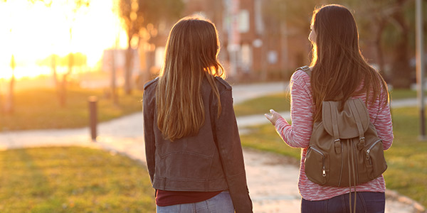 Two friends walking together on a sunny path, enjoying a conversation as the sun sets in the background