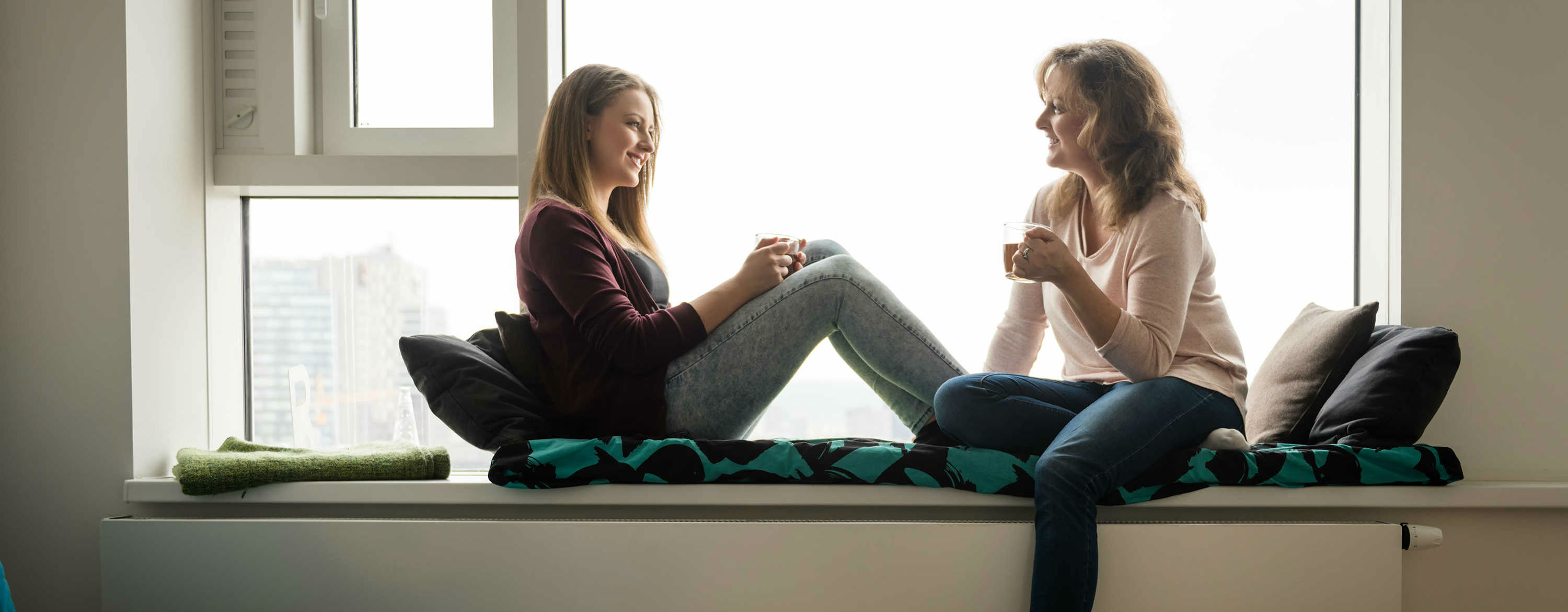 Mother and daughter sitting on a window sill talking to each other.