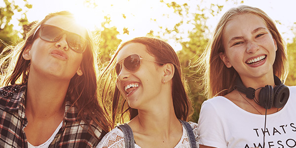 Three smiling young women wearing sunglasses, enjoying a sunny day outdoors with laughter and friendship