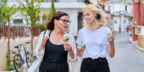 Mother and daughter are walking down the street, talking and eating ice cream