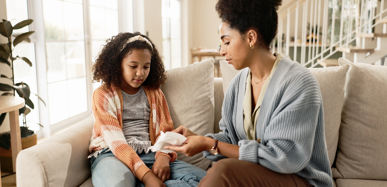 Mother sitting on a sofa showing her young daughter a feminine pad and answering her questions