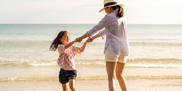 Mother and daughter holding hands and spinning in circles on a sandy beach in summer clothes