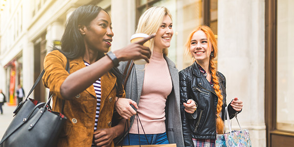 Three friends enjoy a day of shopping while carrying bags and sipping drinks in a vibrant urban setting