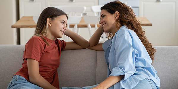 Mother and daughter sitting on the sofa and talking to each other.