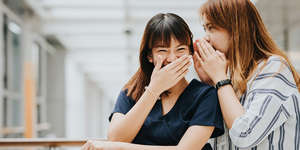 Two friends sharing a secret, laughing together in a bright indoor space, fostering a joyful and intimate moment