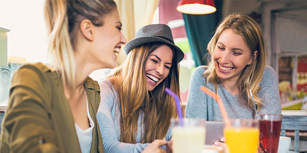 Three women laughing together in a cafe, enjoying colorful drinks, capturing a joyful moment of friendship