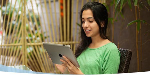 Smiling woman with long hair sitting outdoors, using a tablet while wearing a green shirt in a relaxed environment