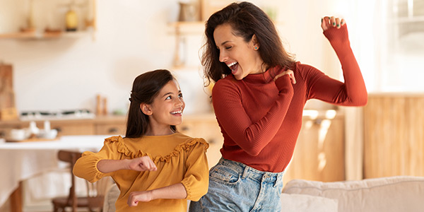 Mother and daughter smiling and dancing in the living room