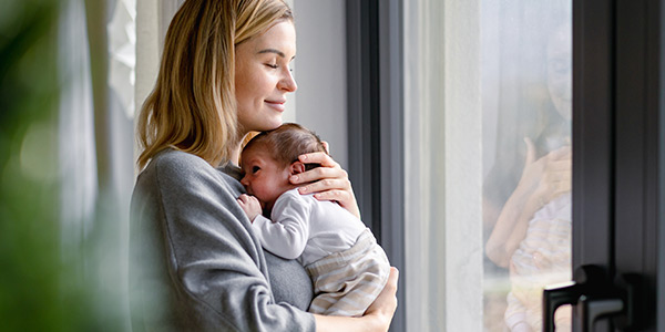 A mother holding on her chest a newborn and standing by the window