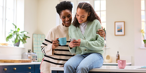 Two women enjoying a moment together in a bright kitchen, sharing smiles while looking at a phone