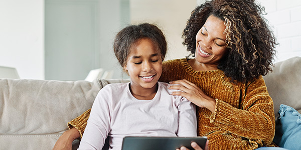 Mother with daughter sitting on couch, smiling and watching on computer