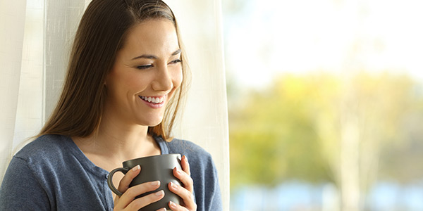 A woman with long brown hair smiling while holding a cup of coffee.