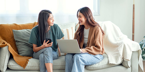 Two girls sitting on the sofa in the living room and talking to each other.