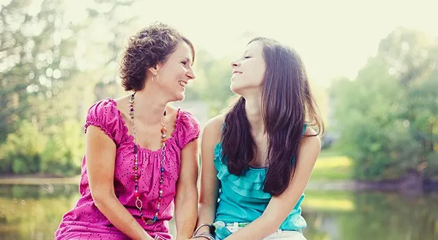 Two women smiling at each other holding hands outdoors, showcasing a happy bond and love between them