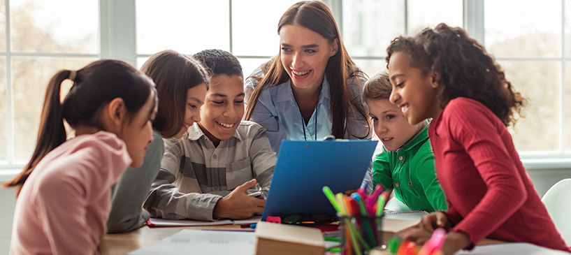 A group of five smiling children with teacher, enjoying their time in class