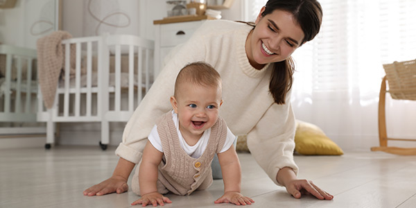 A joyful mother watches her smiling baby crawling on the floor in a bright, cozy living room