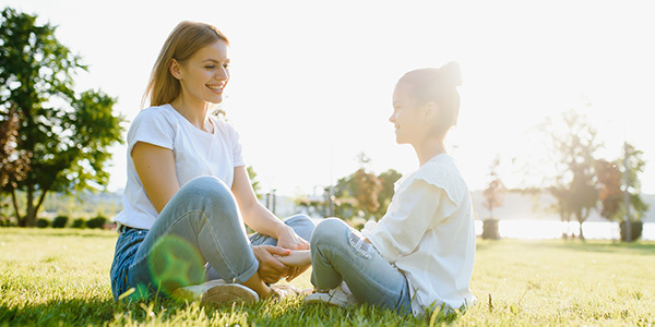 Mother and daughter sitting on the grass field and smiling.