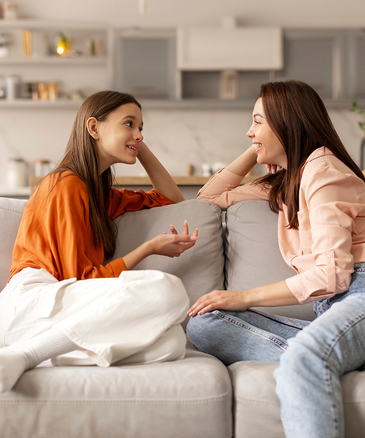 A mother and daughter share a joyful moment while sitting on a couch, engaging in a warm conversation at home