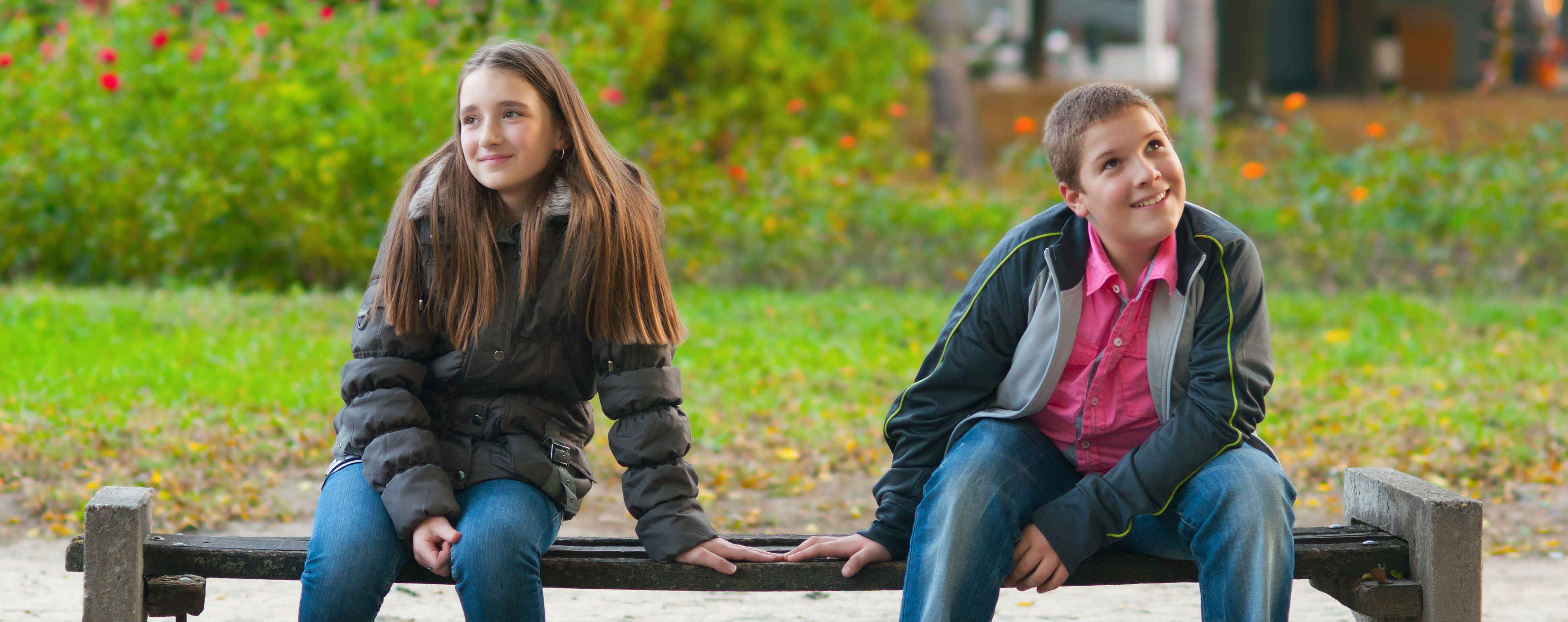 Two children sitting on a bench in a park.