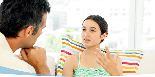 A girl speaks animatedly while sitting on a colorful couch, engaging in a conversation with an adult