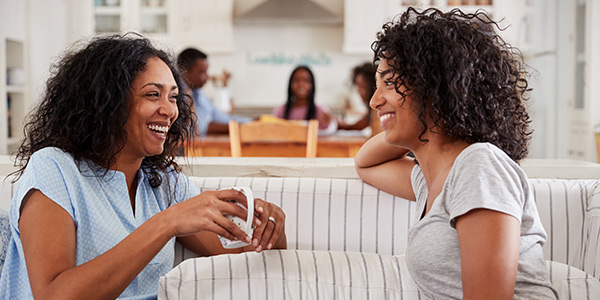 Two smiling women are sitting on the sofa, talking and drinking coffee