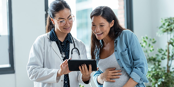 A healthcare professional shows a pregnant woman information on a tablet, both smiling in a bright clinic setting