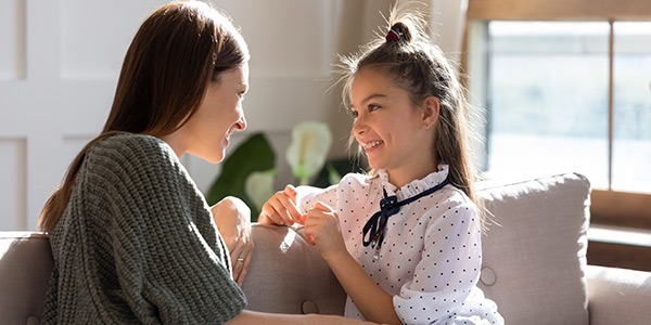 A smiling woman and young girl share a joyful moment on a sofa, surrounded by bright, natural light