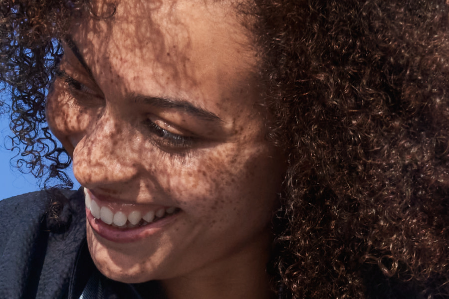 une femme souriante aux cheveux très bouclés regarde sur le côté