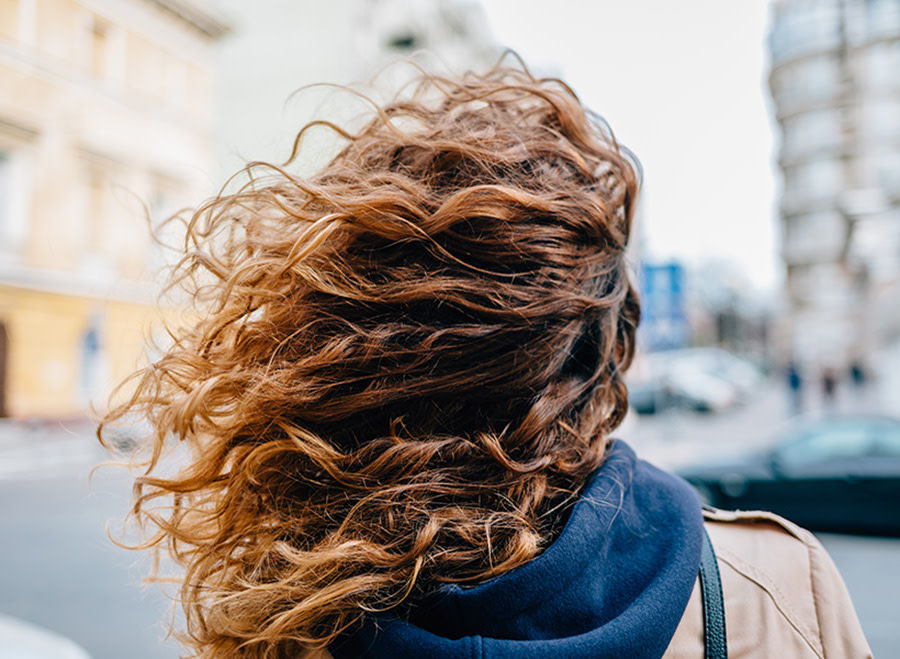 Gros plan de longs cheveux bruns bouclés et ondulés, montrant une texture riche et du volume.