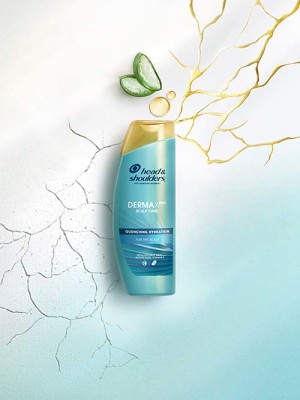 Le shampooing Derma X Pro posé sur une surface crantée bleu sable entourée d'aloès coupé et de gouttes d'huile