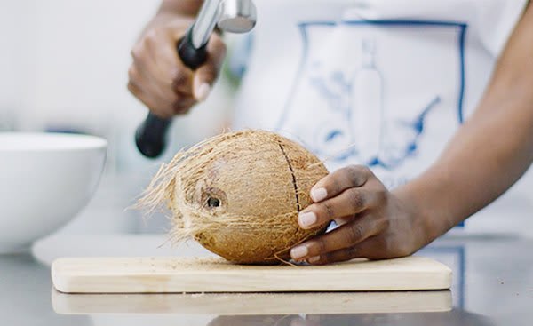 femme qui coupe une noix de coco sur planche à couper