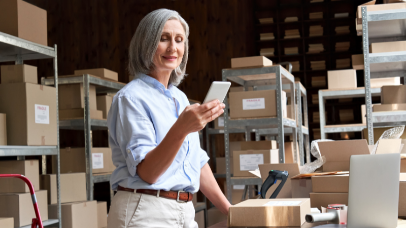 Woman in warehouse using mobile to manage her workload