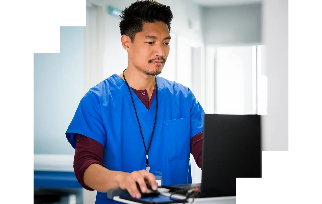 Male nurse using laptop in hospital corridor