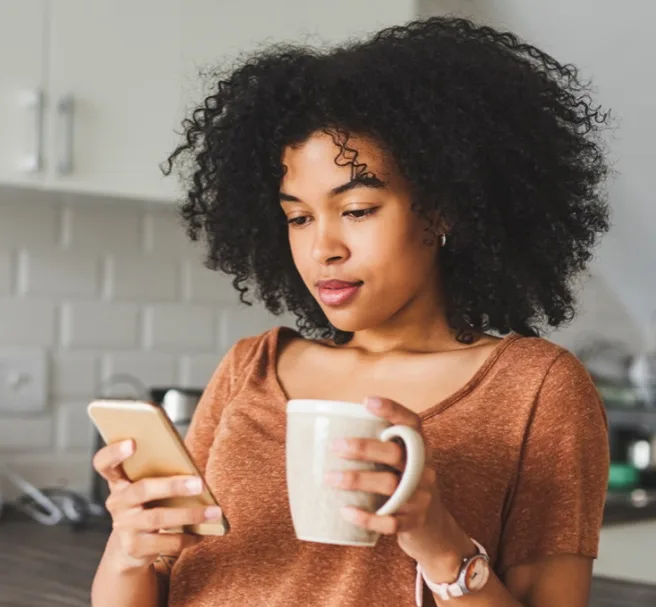Woman looking at phone while drinking coffee