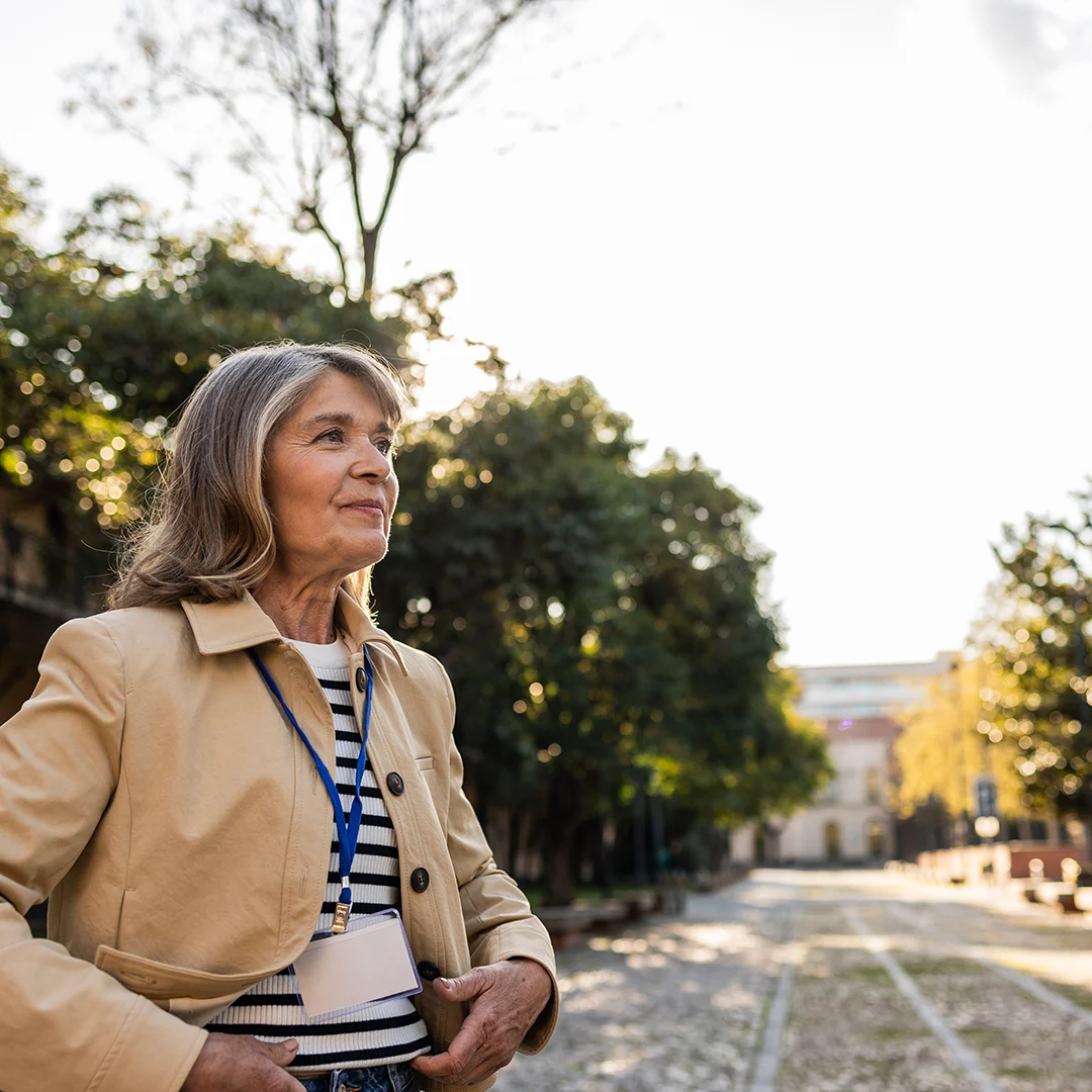 Middle-aged woman standing in the road of a university campus looking optimistically toward the distance.