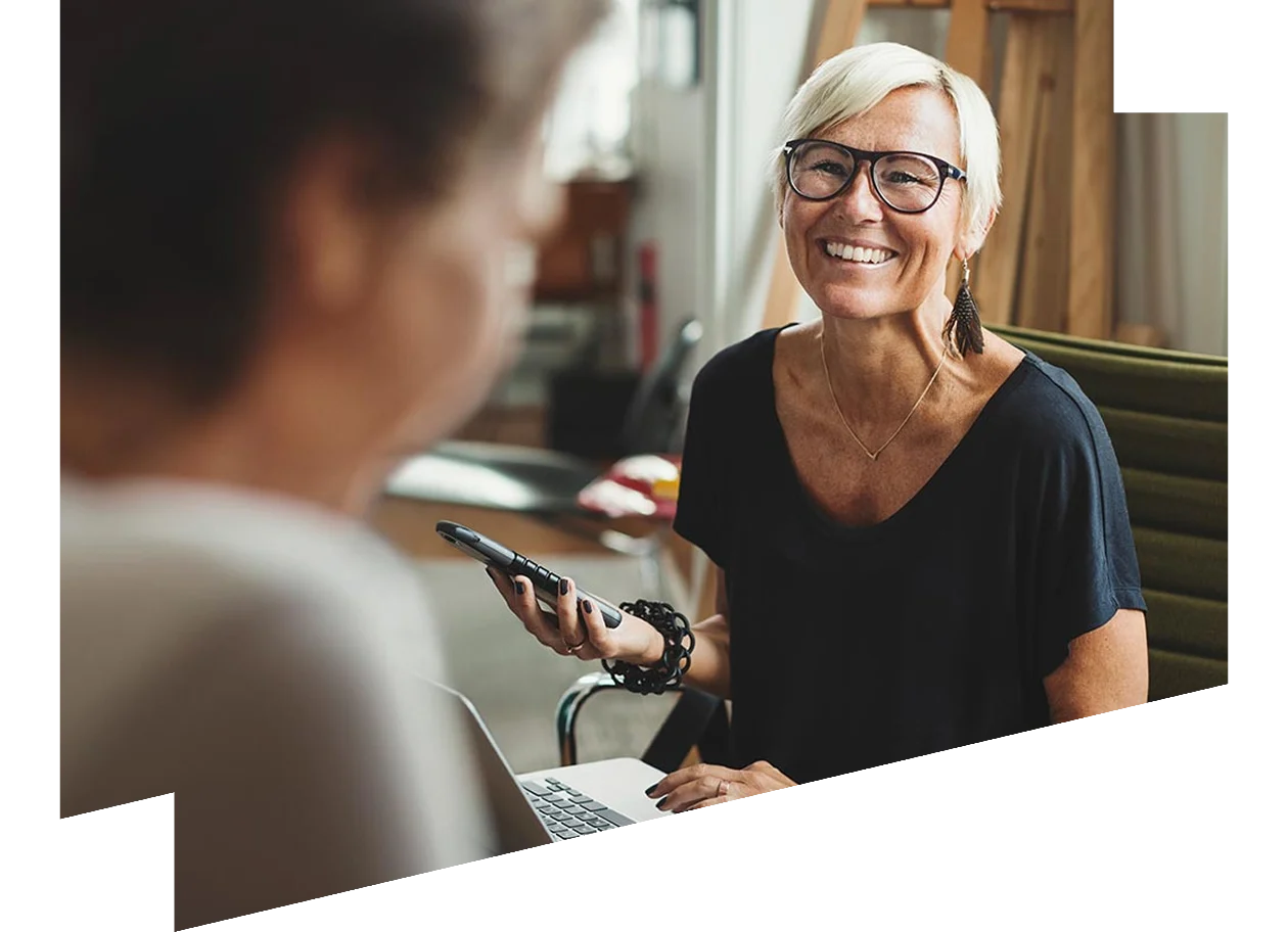 Woman with a laptop and phone smiling at a colleague