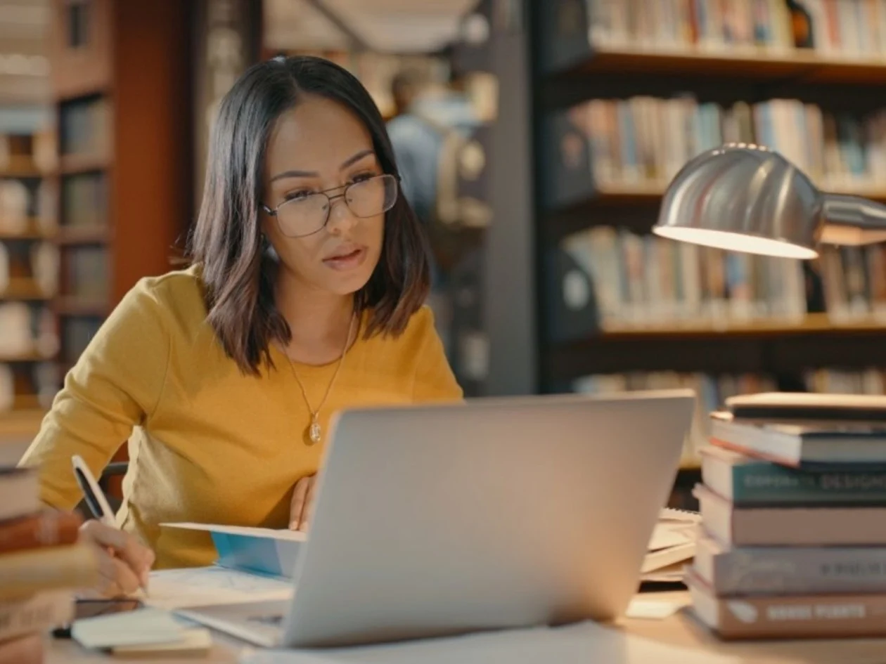 Woman in library studying books and on a laptop